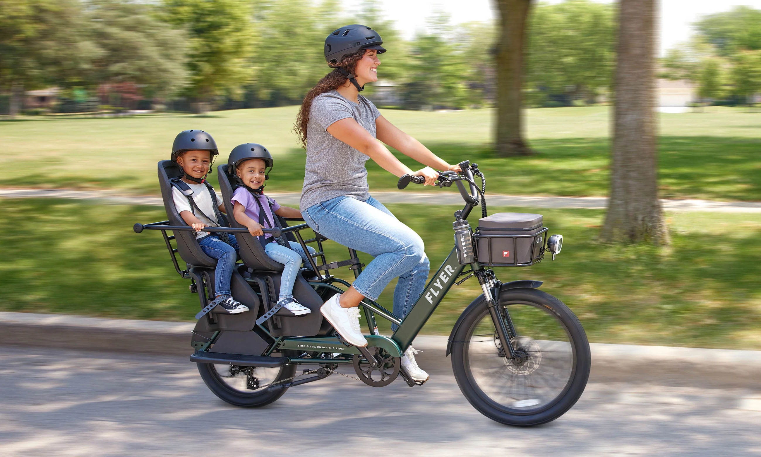 A parent riding a longtail cargo bike with two children on the back