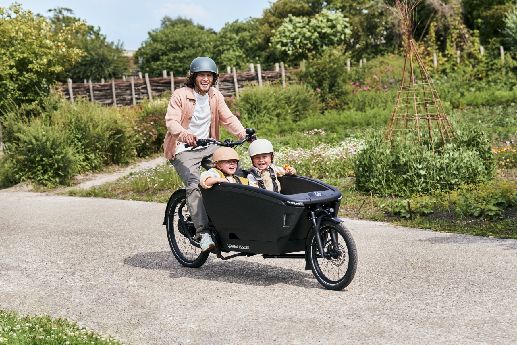 A parent riding a cargo bike with two children in the box