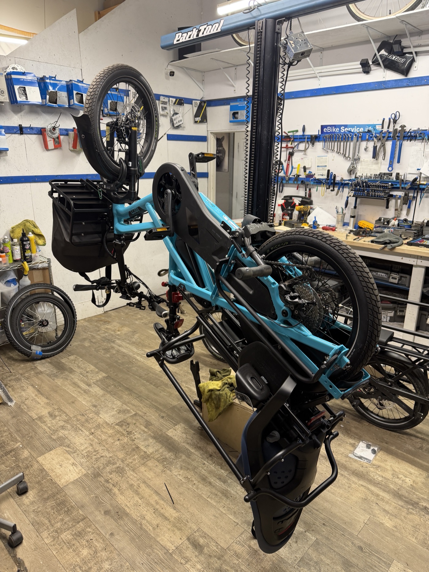 A turquoise cargo bike raised on the service lift inside Front Range Cargo Bikes